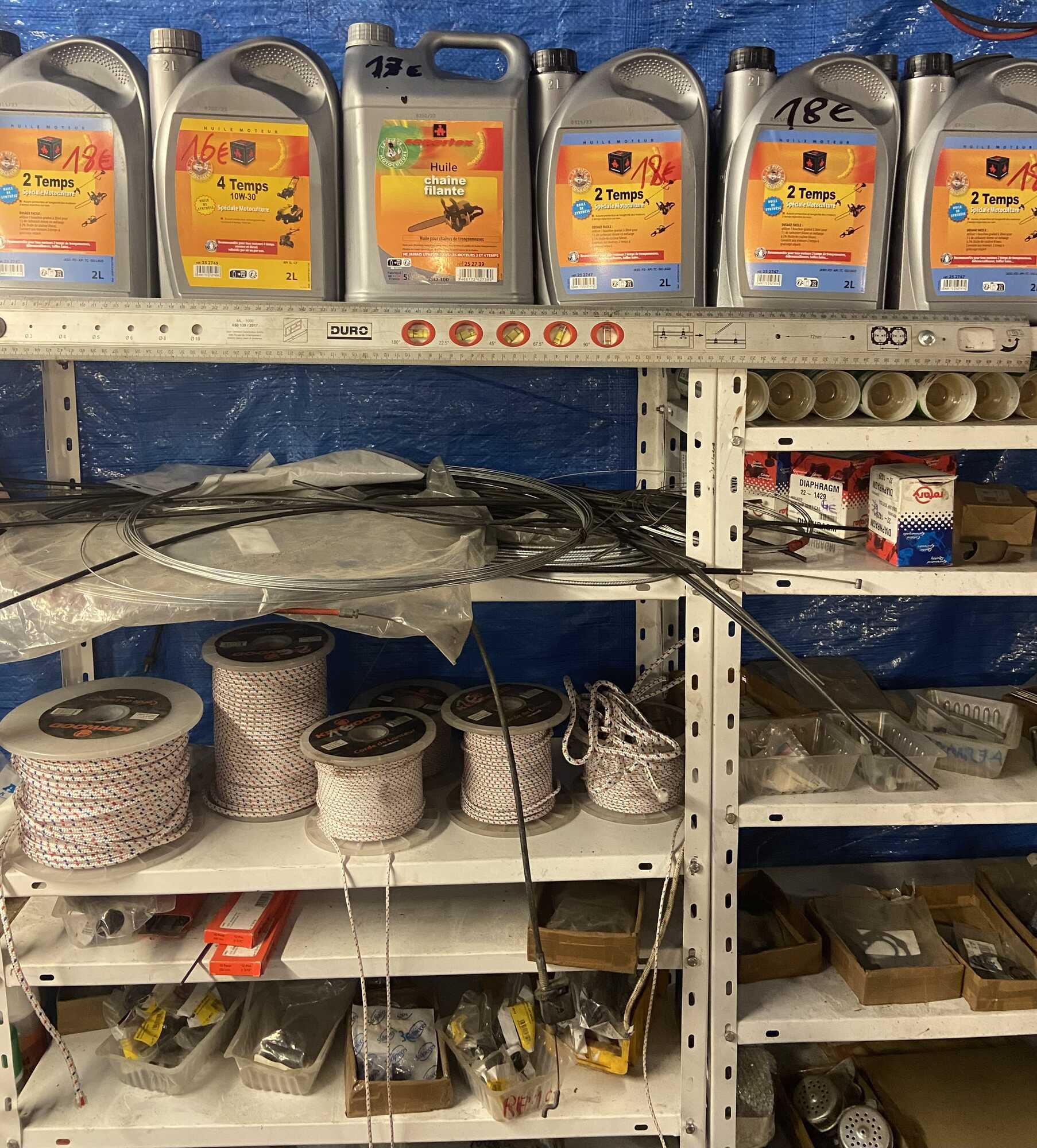 Bidons d’huile et matériel de quincaillerie chez Pezet Motoculture à Laboutarié sur des étagères métalliques blanches,